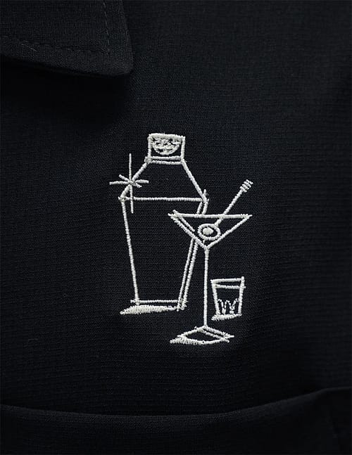 Denne enkelt-panel sorte bowlingskjorte har et broderi af en drinkshaker, en martiniglas og et målebæger på venstre brys